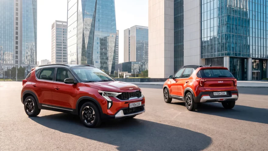 Два красных Kia Sonet Prime на площади среди стеклянных высоток, один спереди сбоку, второй сзади